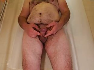 Obese hairy man plays with his dick while standing in bathtub before taking shower
